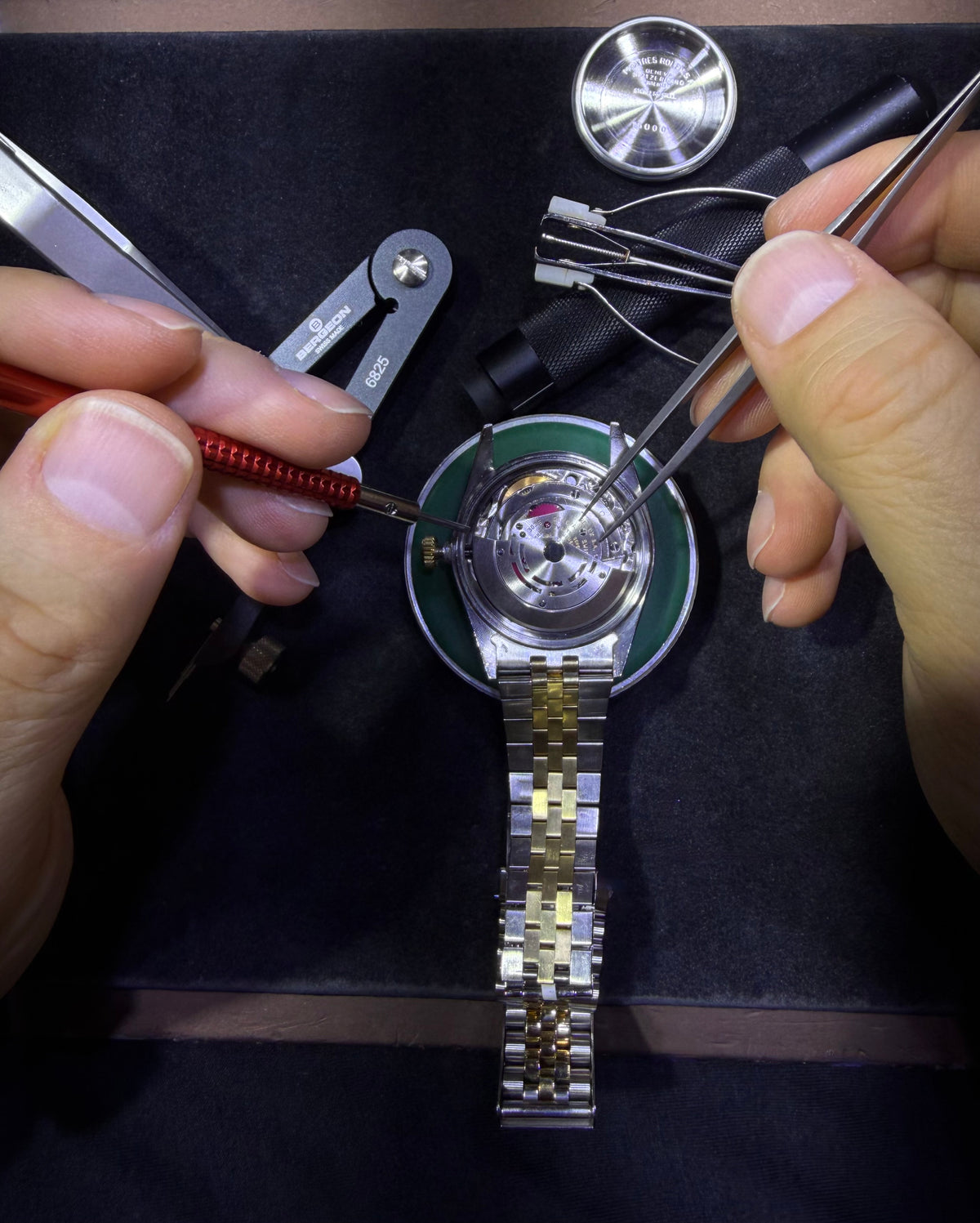 Hands using fine tools to service an open Rolex watch movement.